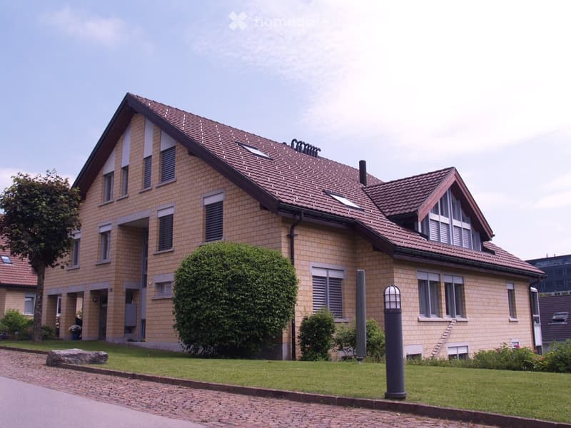 Two-story brick house with a red-tiled roof, multiple windows, and a well-maintained lawn.