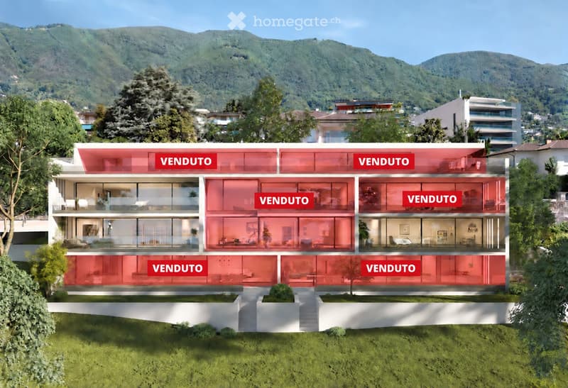 Modern multi-story building with large glass windows and balconies, surrounded by greenery and mountains.