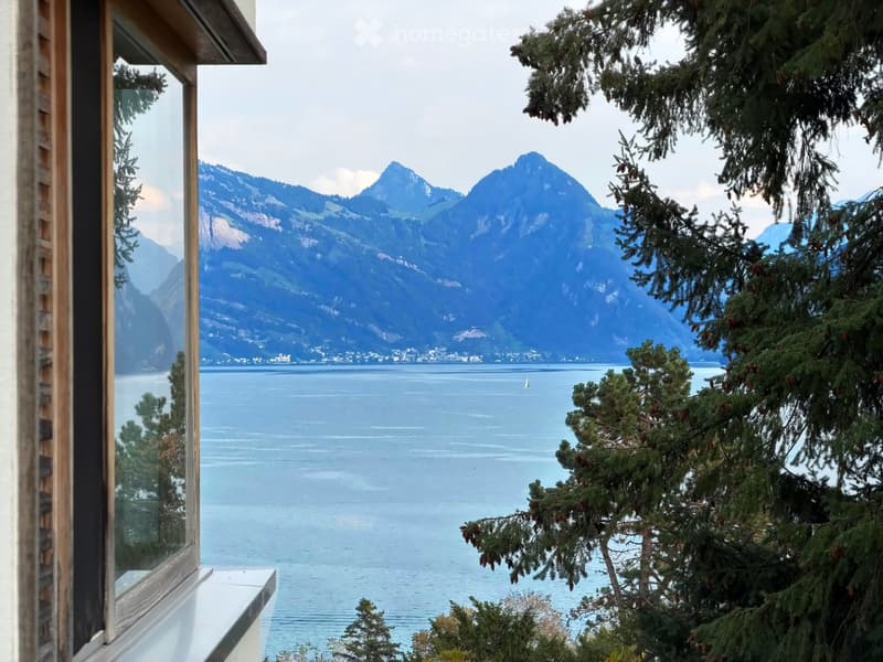 Balcony overlooking a serene lake with distant mountains and a sailboat on the water.