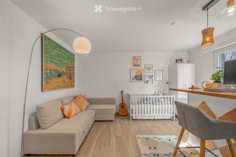 A modern, multi-functional living space with a sofa, baby crib, guitar, desk with laptop, and decorative artwork.