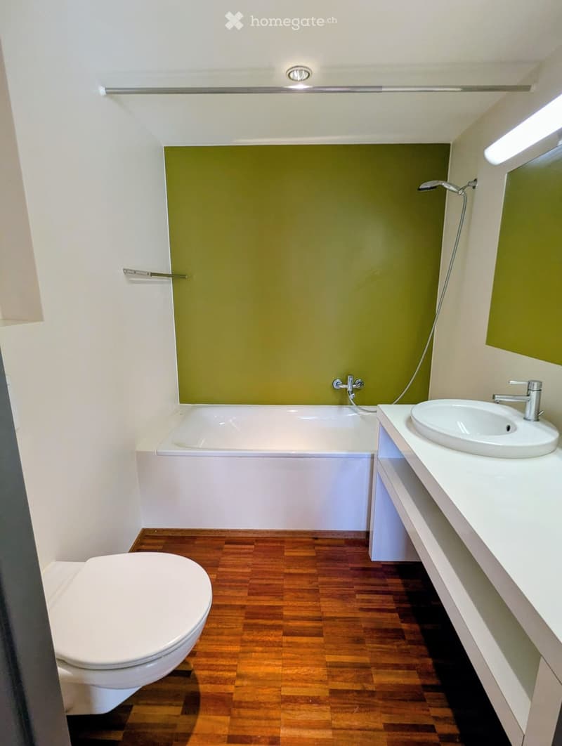 Modern bathroom with a white bathtub, a white sink with a chrome faucet, a toilet, and wooden flooring.