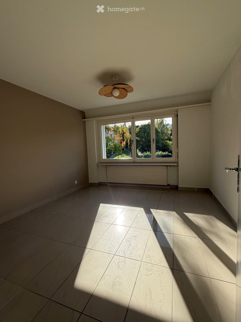 Empty room with tiled floor, large window, radiator, and a ceiling light fixture.