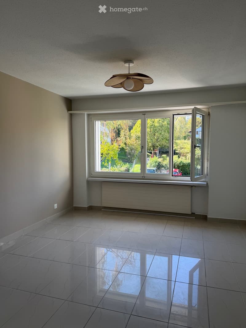 Empty room with large windows, tiled floor, radiator, and a ceiling fan.