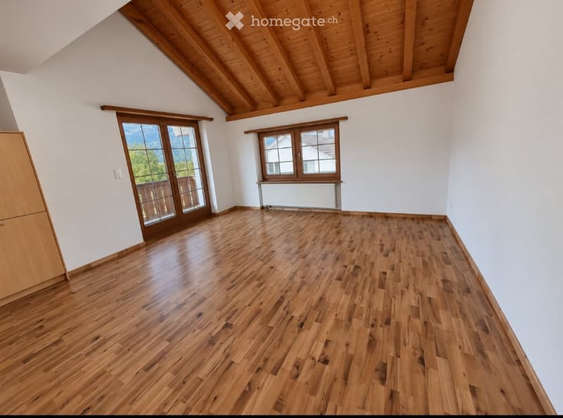Empty room with wooden flooring, white walls, large window, and sliding glass door leading to a balcony.