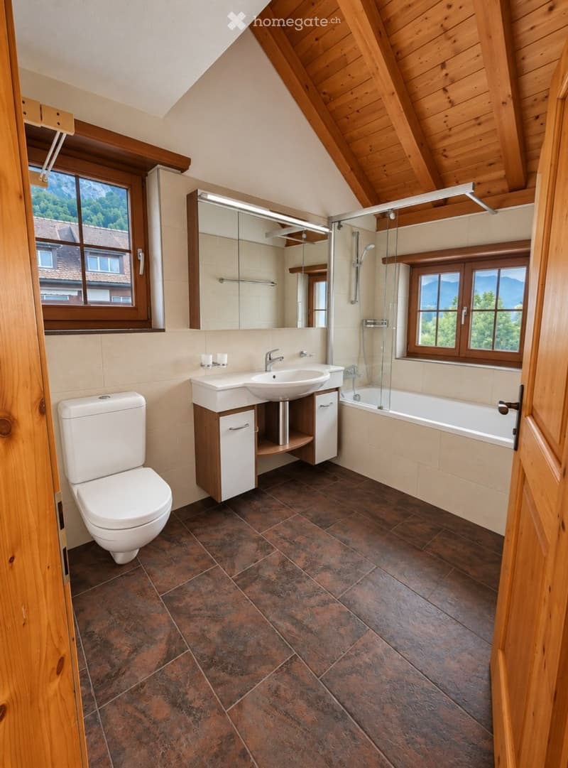Bathroom with wooden ceiling, brown tiled floor, white toilet, sink with cabinet, bathtub with glass shower enclosure, and large windows offering a scenic view.