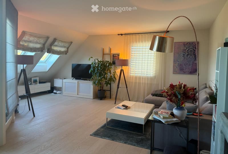 Modern living room with wooden flooring, large windows, and skylights. Features a grey sofa, white coffee table, floor lamp, TV, and decorative plant in a pot.
