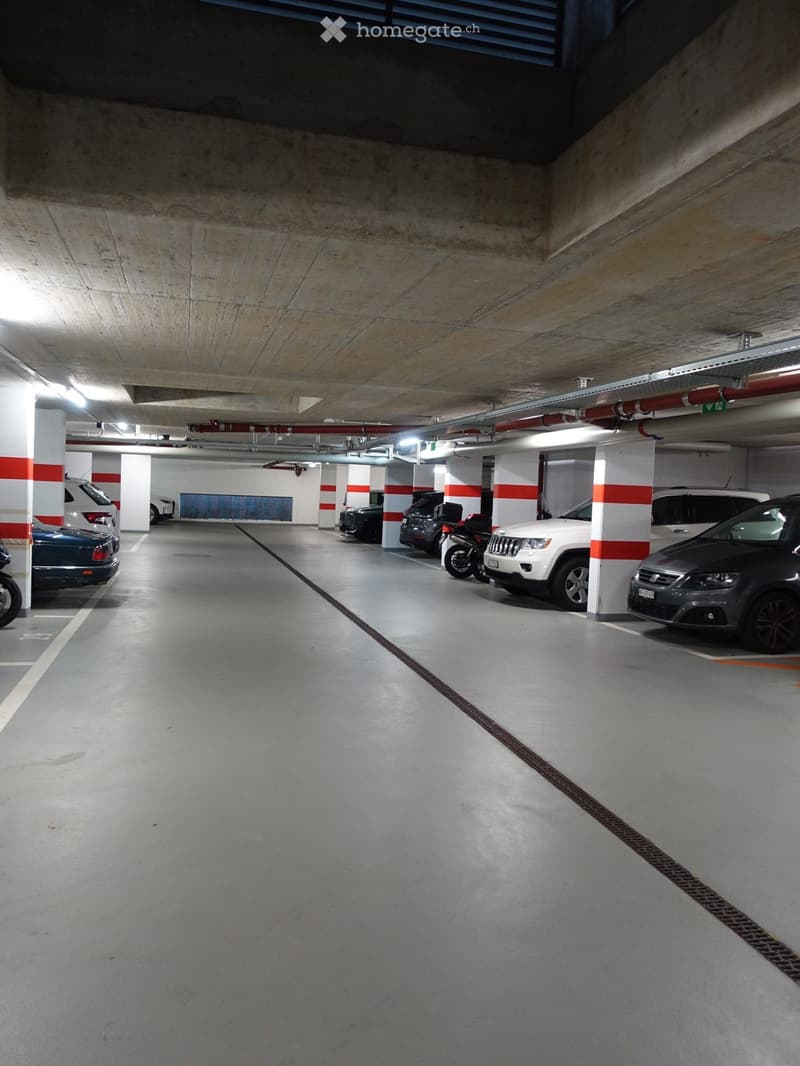 Underground parking area with several parked cars and a motorcycle, concrete pillars, and lighting.