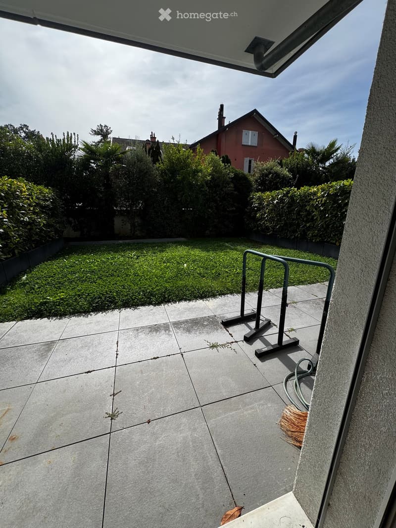 Balcony with concrete tiles, small grassy area, metal railing, and a broom leaning against the wall.