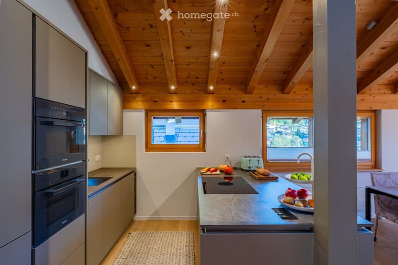 Modern kitchen with wooden ceiling beams, stainless steel appliances, granite countertops, and a variety of fresh fruits and vegetables on the counter.