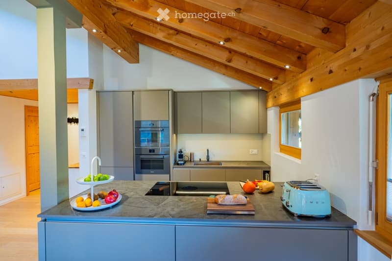 Modern kitchen with wooden beams, stainless steel appliances, and a marble countertop. Features include an oven, sink, toaster, and fresh fruits on the counter.