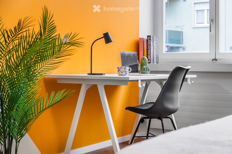 A modern, minimalist workspace with a white desk, black chair, laptop, cup, cactus, books, and a small lamp. The room features a bright yellow accent wall and a large window with a view.