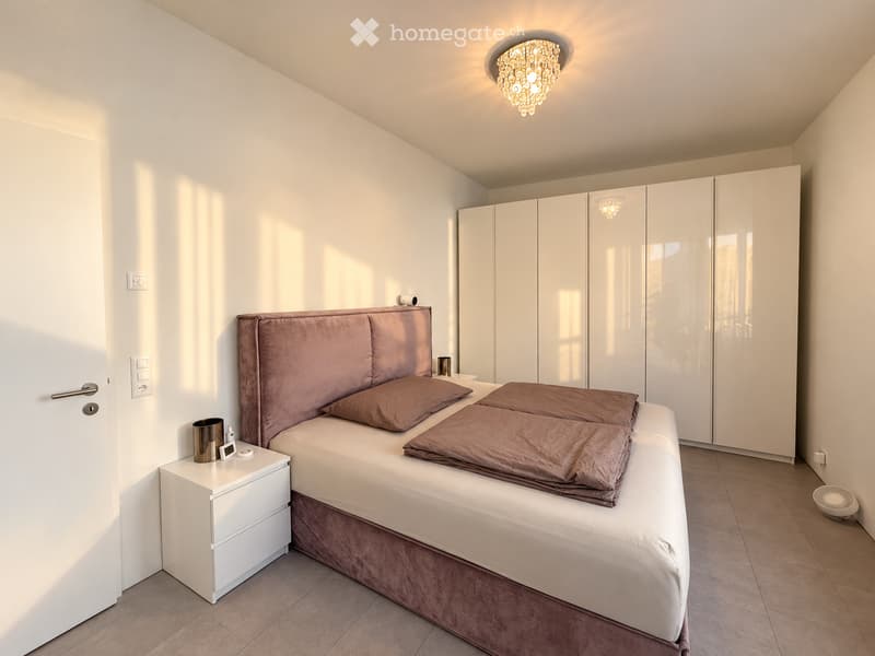 Modern bedroom with a large bed, nightstand, wardrobe, and decorative lighting.