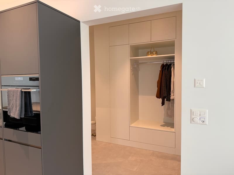 Modern built-in wardrobe with integrated oven, shelves, and hanging space for clothes. Light switches on the wall.