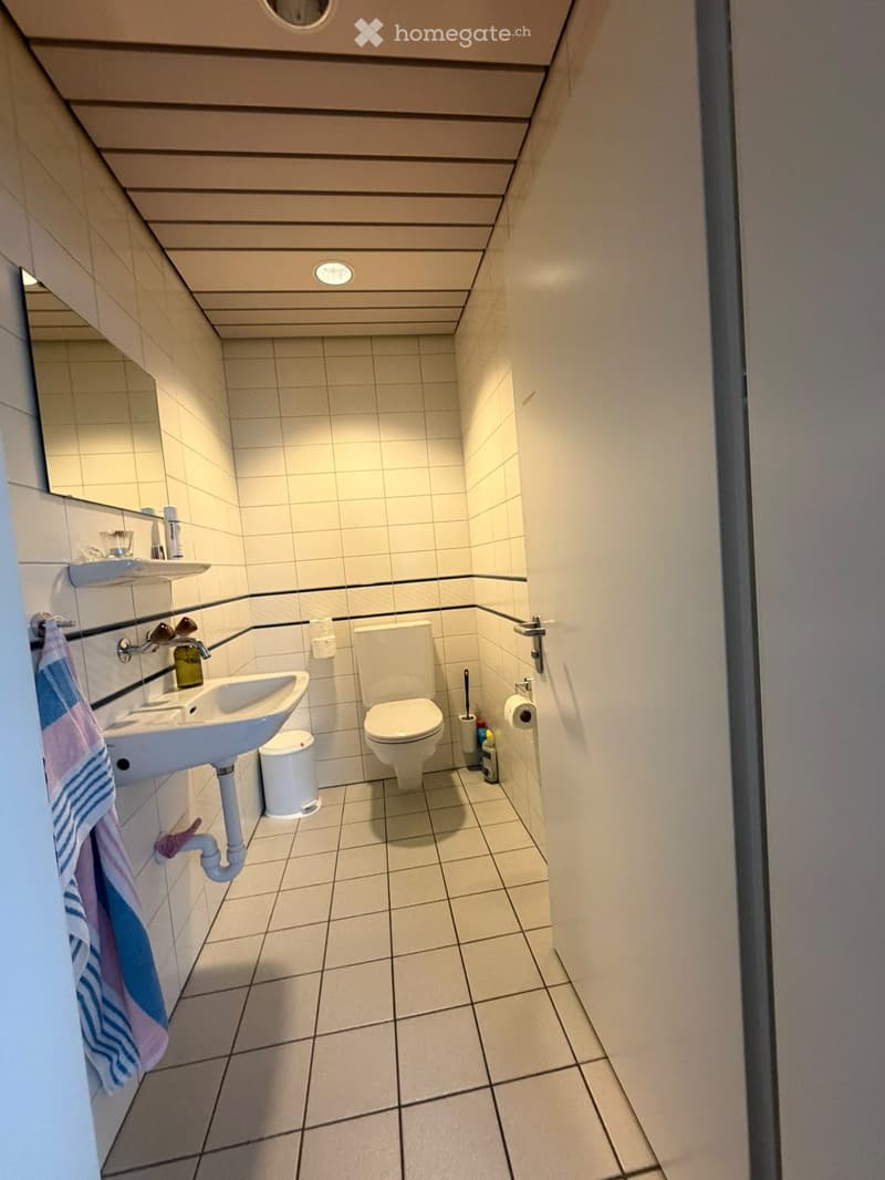 Modern bathroom with white tiles, a sink, toilet, mirror, and a towel hanging on a rack.