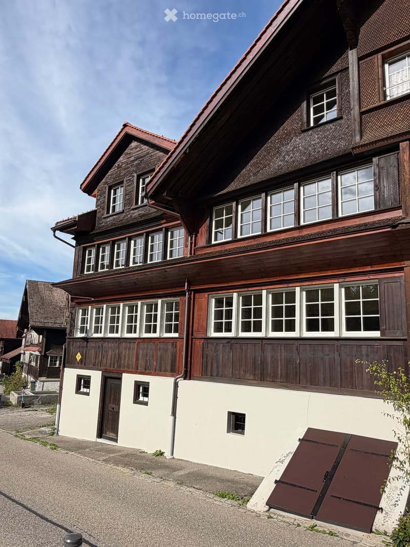 Traditional two-story wooden house with a steeply pitched roof, multiple windows, and a raised ground floor.