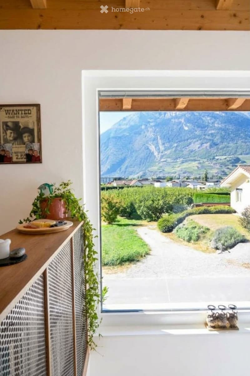 Bright room with large window offering a scenic mountain view, featuring a wooden cabinet with a plant, a plate, and a teapot on top.