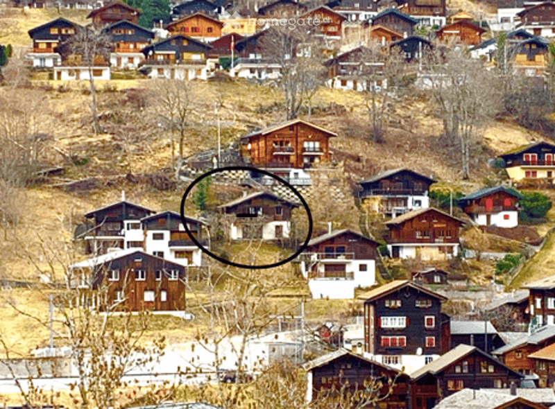 Aerial view of a village with multiple houses on a hillside, featuring wooden and stone structures with balconies and windows.
