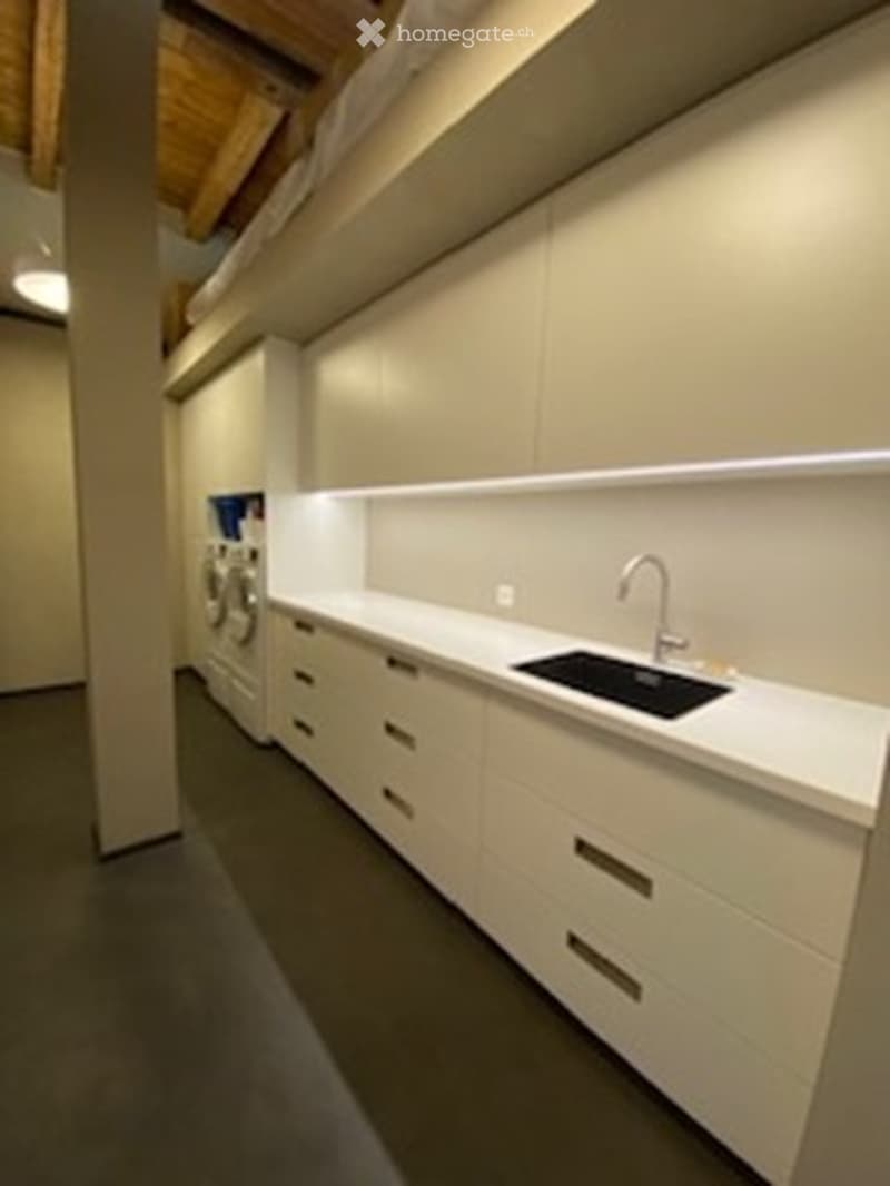 Modern kitchen with white cabinets, a sink, and a faucet. The space features a clean, minimalist design with a visible washing machine in the background.
