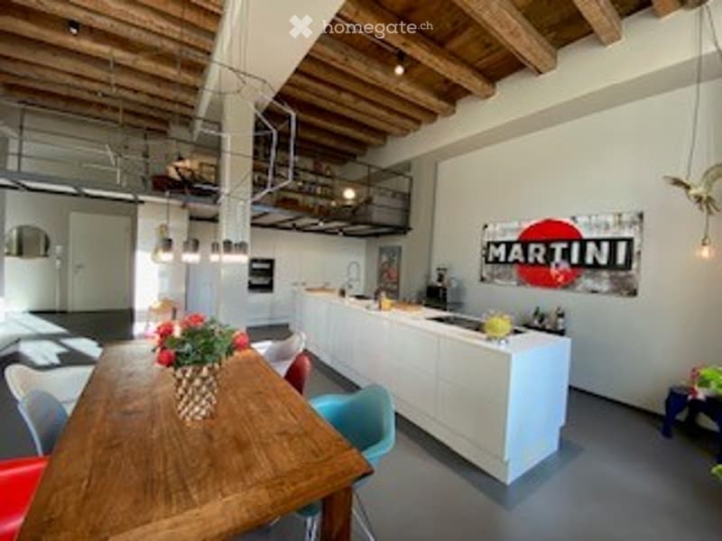 Open-plan living and dining area with a wooden dining table, vase with flowers, kitchen island, and a poster on the wall.