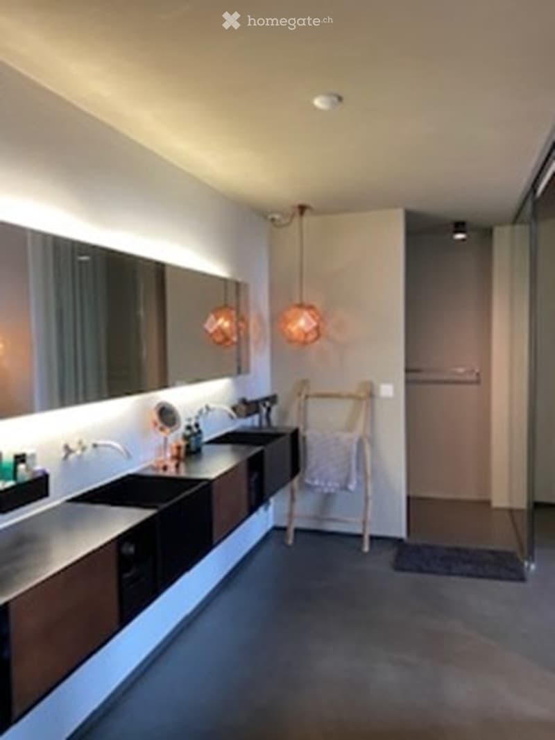 Modern bathroom with sleek black sinks, large mirrors, warm pendant lights, and a towel rack with a folded towel.