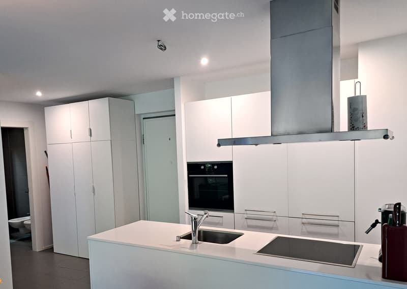 Modern kitchen with white cabinets, stainless steel appliances, island with sink and faucet, and a built-in oven.