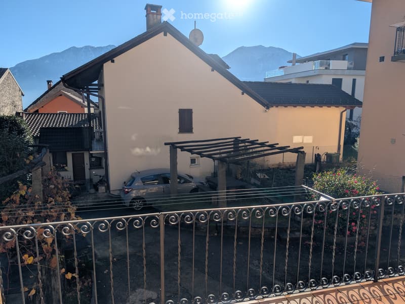 Balcony overlooking a residential area with houses, a parked car, and distant mountains under a clear blue sky.