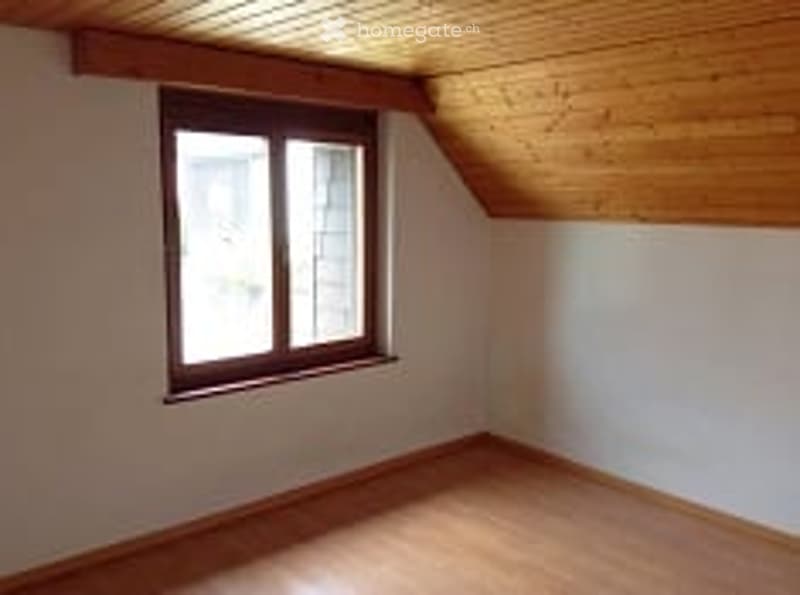 Completely empty room with wooden floor, white walls, and a single window with wooden frame.