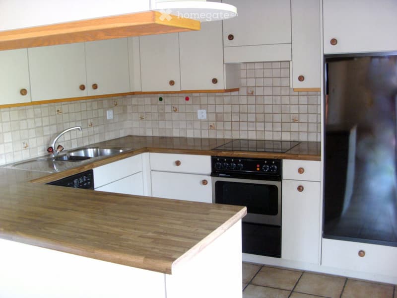 Modern kitchen with white cabinets, wooden countertops, stainless steel sink, and built-in oven and refrigerator.