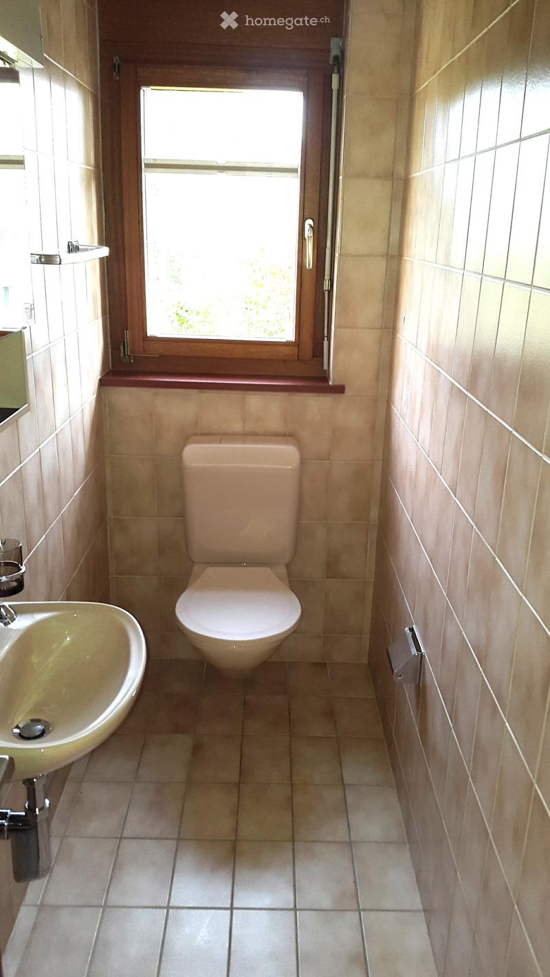 Small bathroom with beige tiles, a toilet, a sink, and a window with wooden frame.