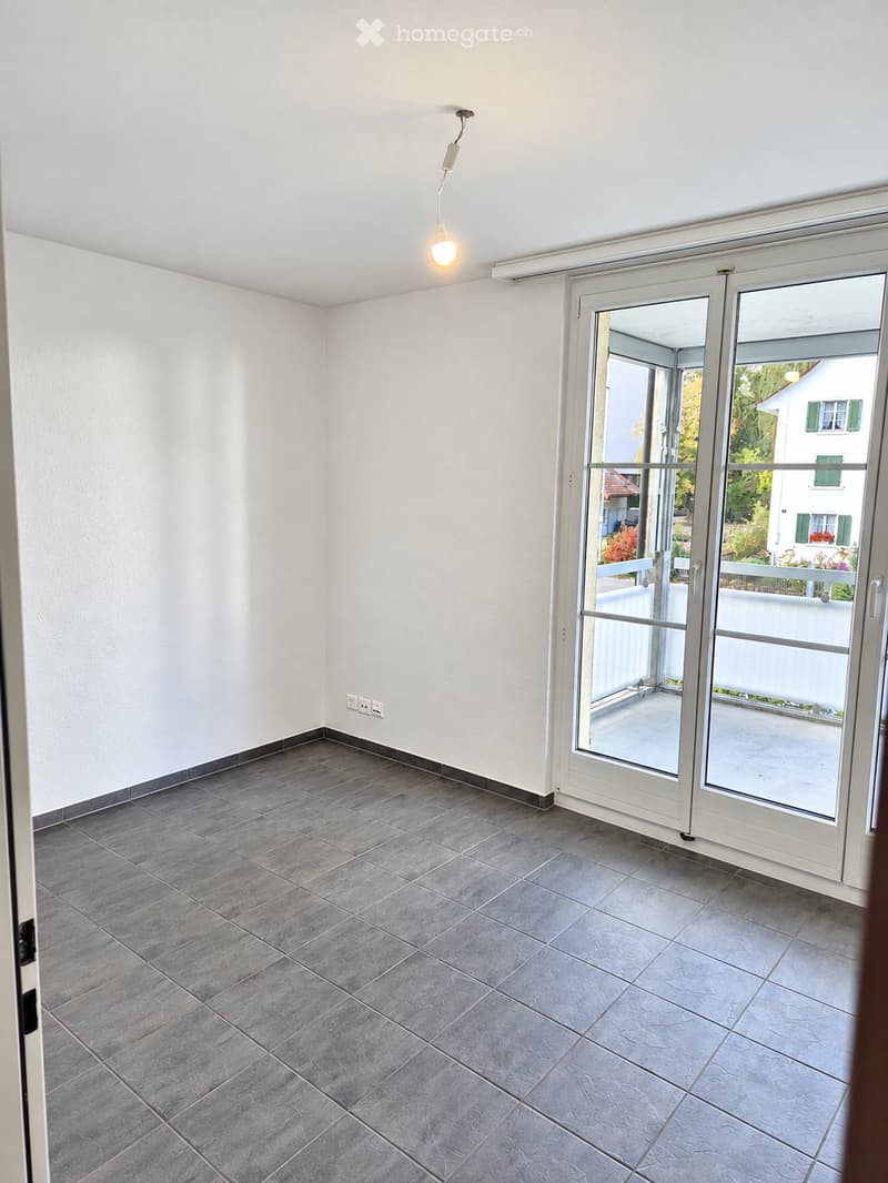 Empty room with grey tiled floor, white walls, and large sliding glass doors leading to a balcony.