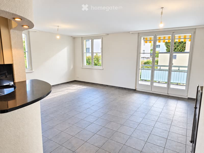 Empty room with tiled floor, white walls, large windows, and a sliding glass door leading to a balcony.