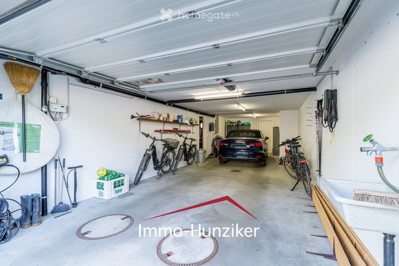 {"type": "Garage", "objects": ["bicycle", "car", "broom", "shelves", "tools", "storage boxes"], "description": "A well-lit garage with a concrete floor, white walls, and a raised ceiling. Contains bicycles, a car, shelves with tools and supplies, and vari