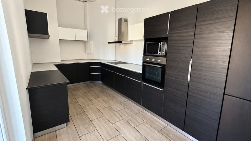 Modern kitchen with dark wood cabinets, white countertops, and stainless steel appliances including an oven, microwave, and range hood.