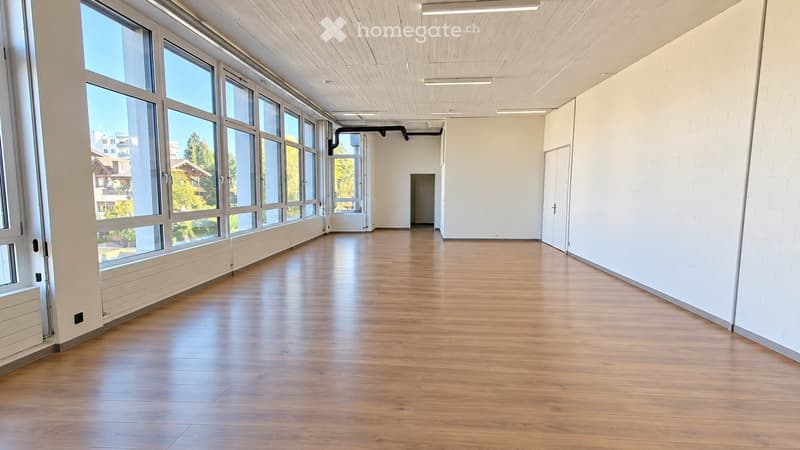 Empty room with wooden flooring, large windows, white walls, and a door leading to another space.