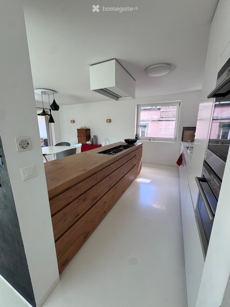 Modern kitchen with a wooden island, induction cooktop, built-in oven, microwave, and a small dining area with a table and chairs.