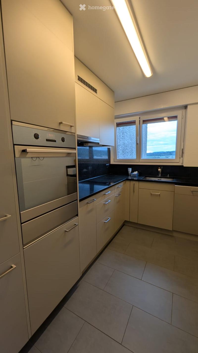 Modern kitchen with light-colored cabinets, stainless steel oven, black countertop, and a window offering a view.