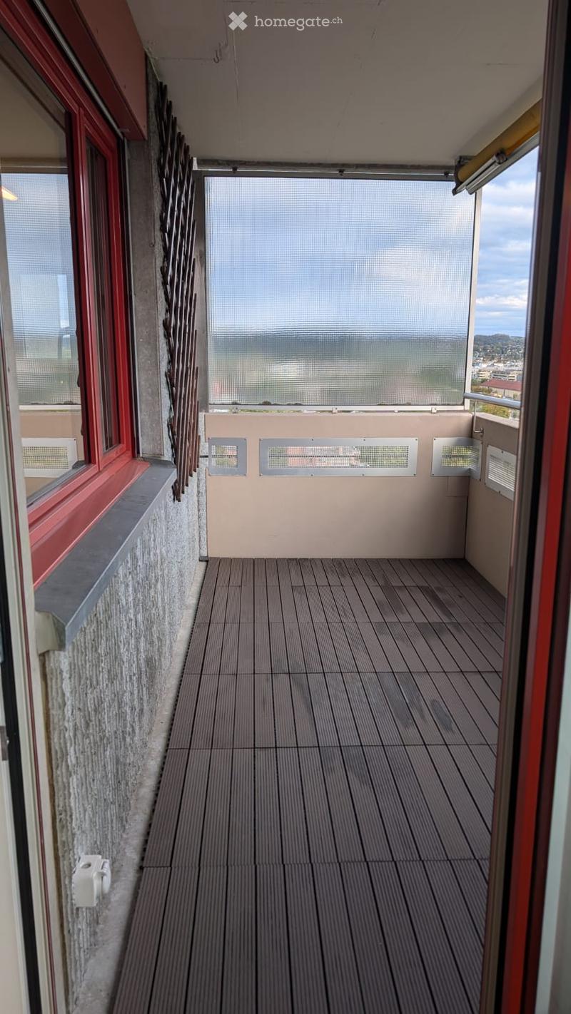 Balcony with wooden decking, large windows, and a view of the city and mountains.