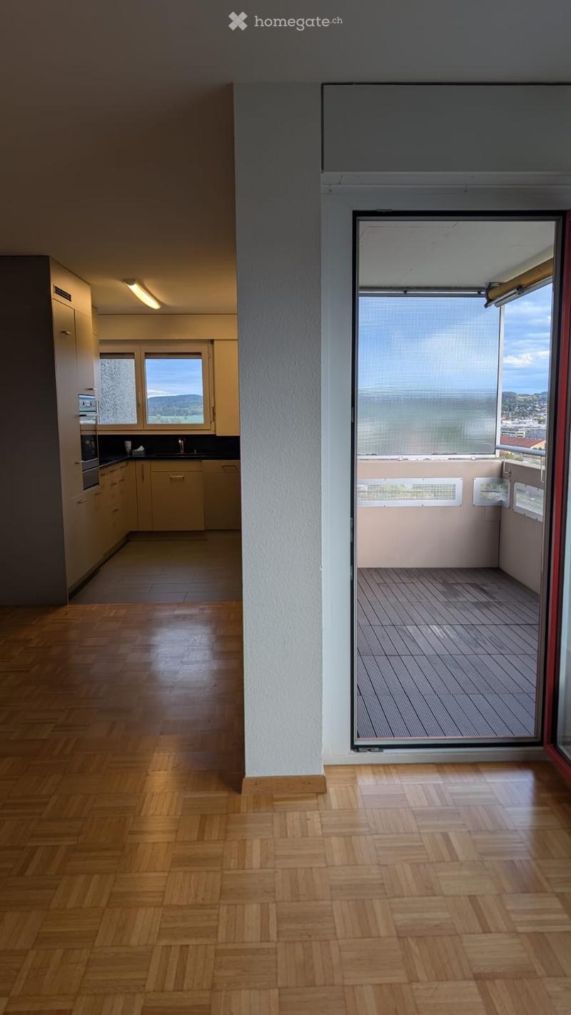 Bright, unfurnished room with wooden flooring, large windows, and a balcony with scenic views.