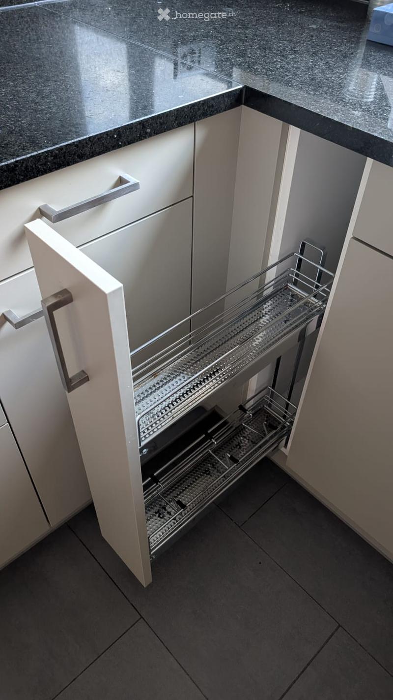 Modern kitchen with white cabinets, a dark granite countertop, and an open drawer revealing a stainless steel cutlery organizer.