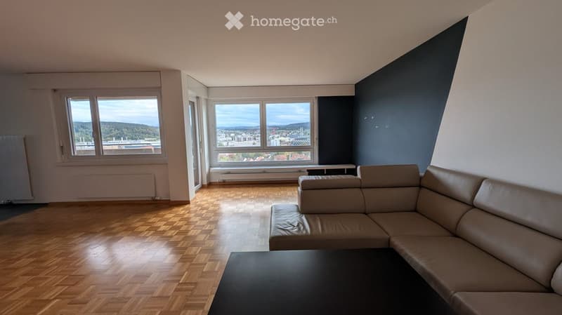 Modern living room with wooden flooring, large windows offering a scenic view, a beige leather sofa, and a black coffee table.