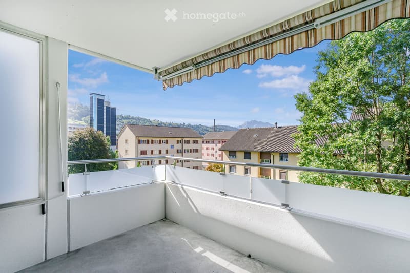 Balcony with white railings, striped awning, and scenic view of city buildings and mountains.