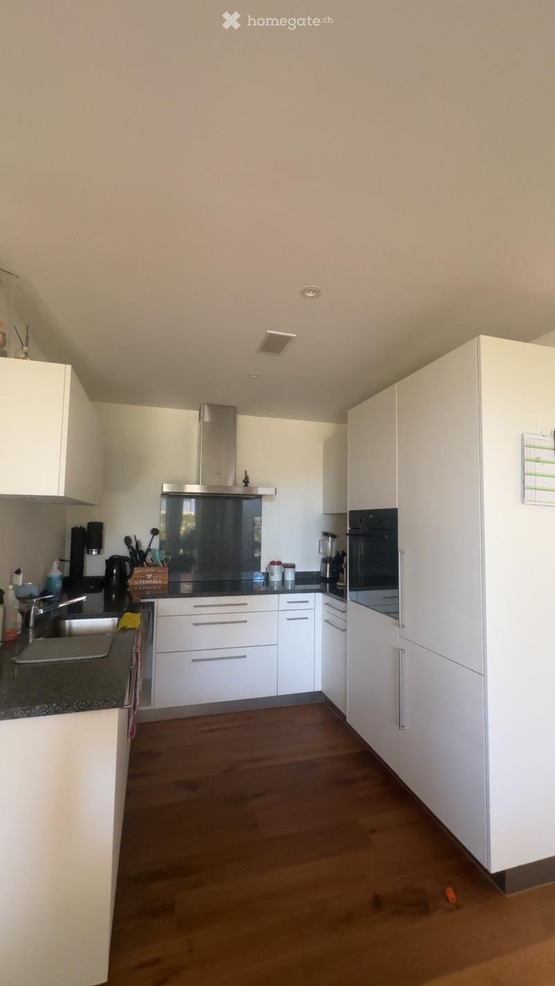Modern kitchen with white cabinets, stainless steel appliances, wooden flooring, and granite countertops.