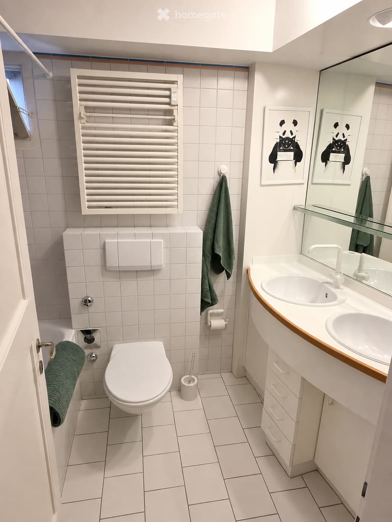 Bathroom. Modern bathroom with white tiles, a toilet, a double sink with a mirror, a radiator, and two green towels.