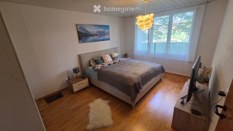 Cozy bedroom with a large bed, nightstand, lamp, screen, picture frame, and a white rug on the wooden floor.