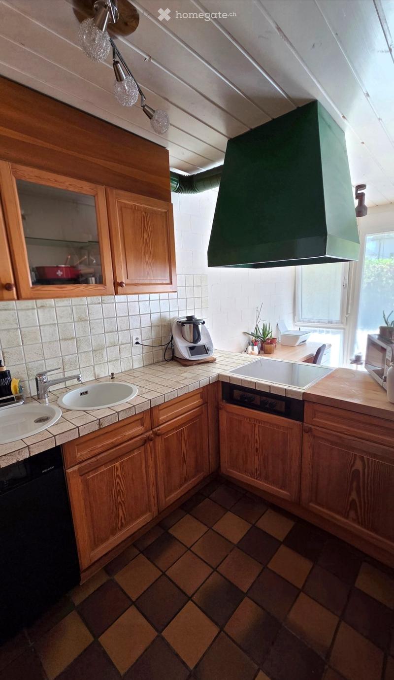 Cozy kitchen with wooden cabinets, tiled countertops, and various appliances including a sink, oven, dishwasher, and microwave. The space features a window and a hanging light fixture.