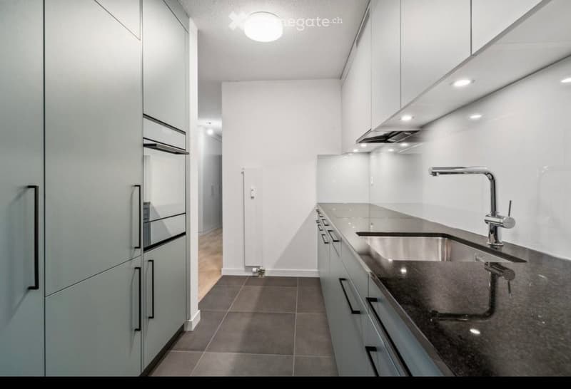 Modern kitchen with white cabinets, stainless steel sink, and sleek faucet. The space features a clean, minimalist design with a dark countertop and tiled floor.