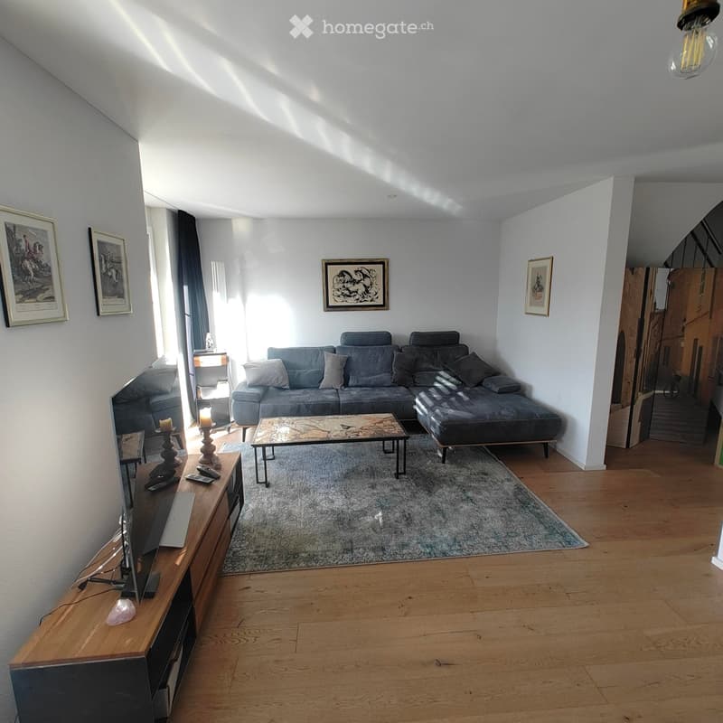 Bright living room with wooden flooring, a grey sectional sofa, coffee table, TV stand, and decorative candles.