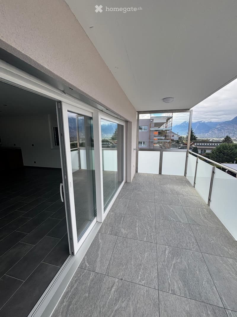Modern balcony with large glass sliding doors, tiled flooring, and a scenic mountain view.
