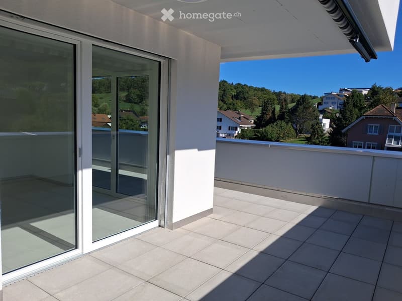 Modern balcony with large glass sliding doors, tiled floor, and a scenic view of a green landscape and houses.
