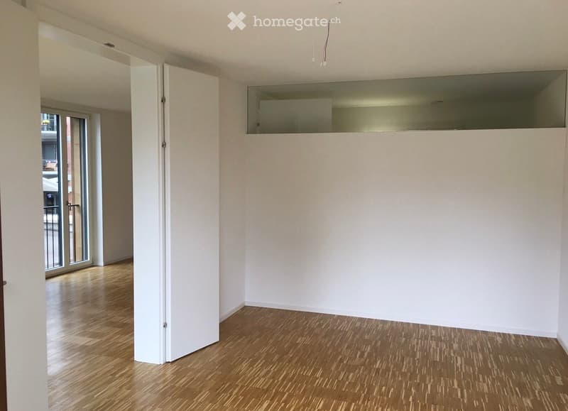 Empty room with wooden flooring, white walls, and a large glass door leading to a balcony.